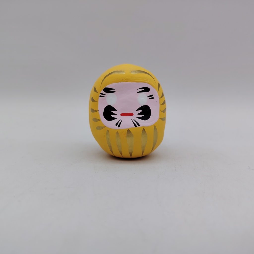Bambola Daruma gialla tradizionale giapponese, vista frontale con dettagli del volto stilizzato e corpo tondeggiante