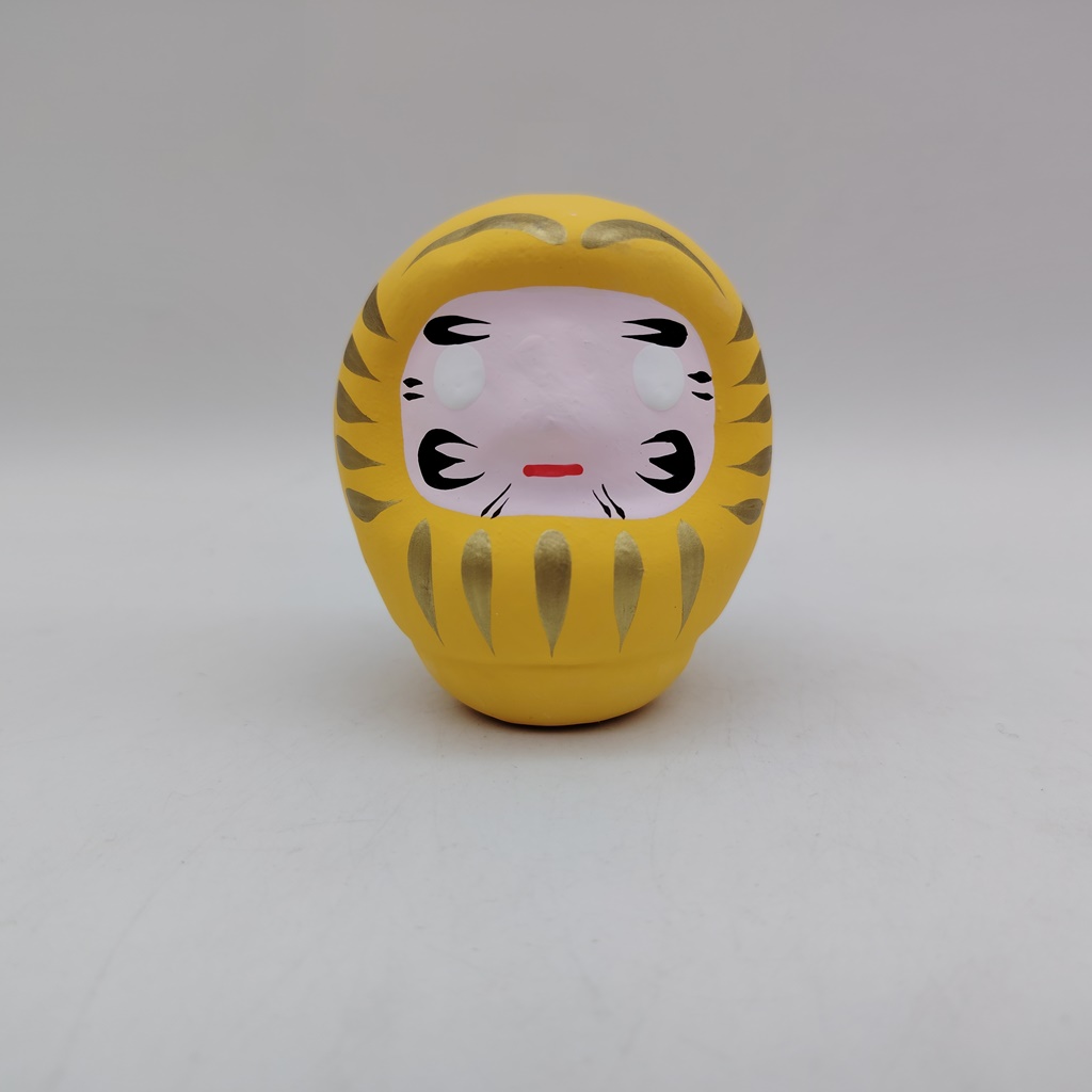 Bambola Daruma gialla tradizionale giapponese, vista frontale con dettagli del volto stilizzato e corpo tondeggiante