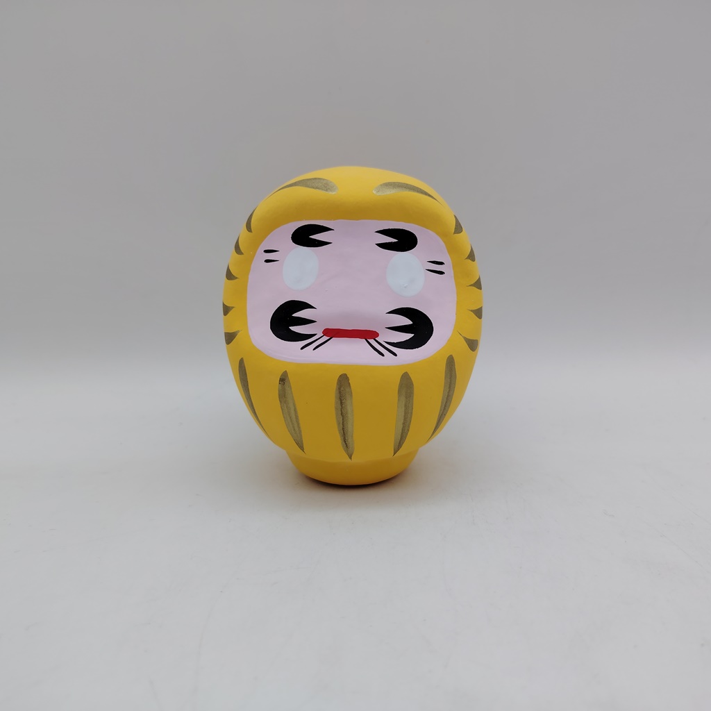 Bambola Daruma gialla tradizionale giapponese, vista frontale con dettagli del volto stilizzato e corpo tondeggiante