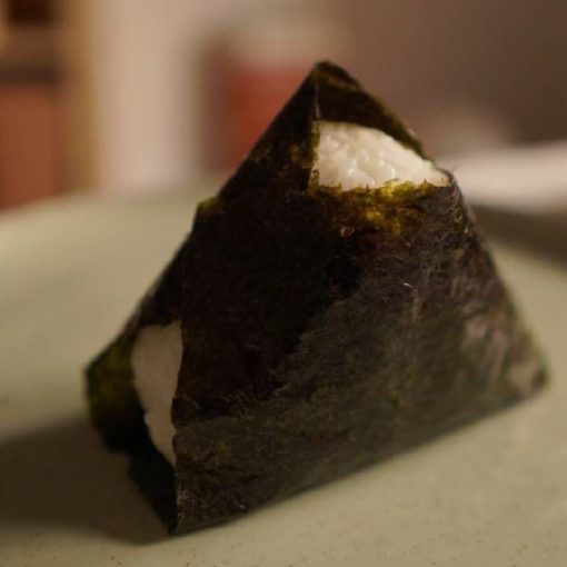 Un onigiri perfettamente modellato, avvolto in un foglio di alga nori scura, pronto per essere gustato.