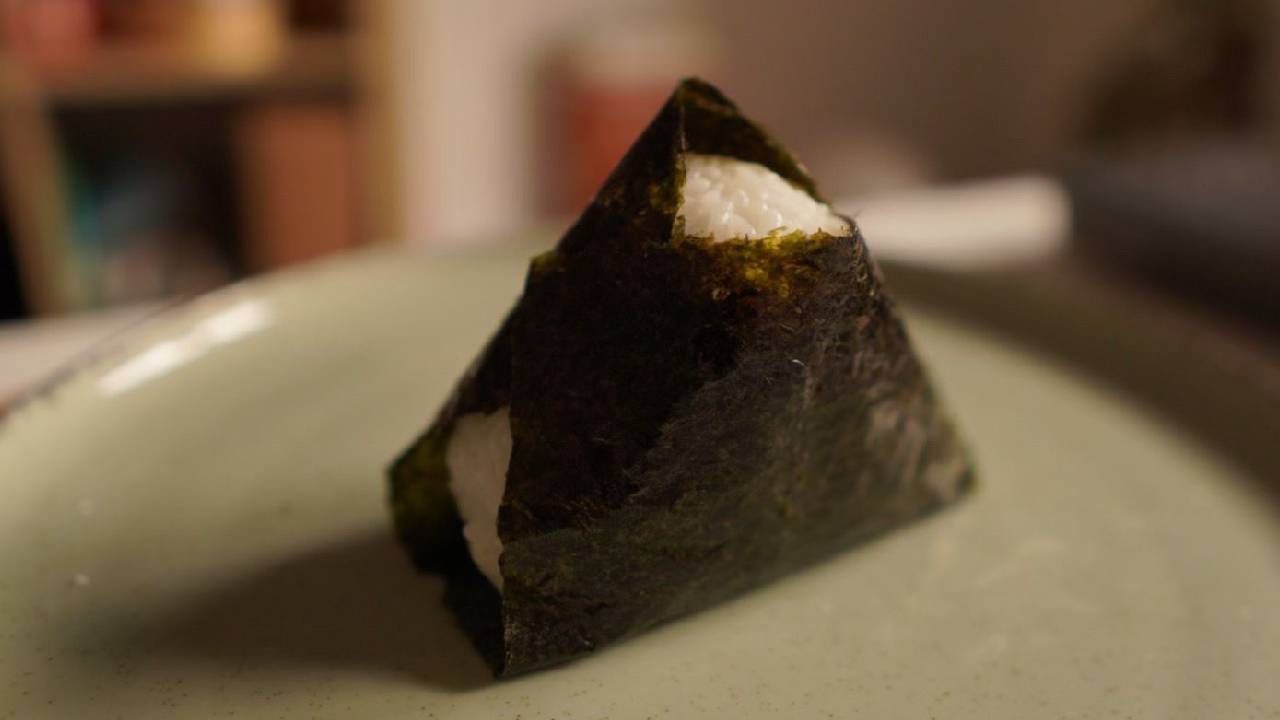 Un onigiri perfettamente modellato, avvolto in un foglio di alga nori scura, pronto per essere gustato.
