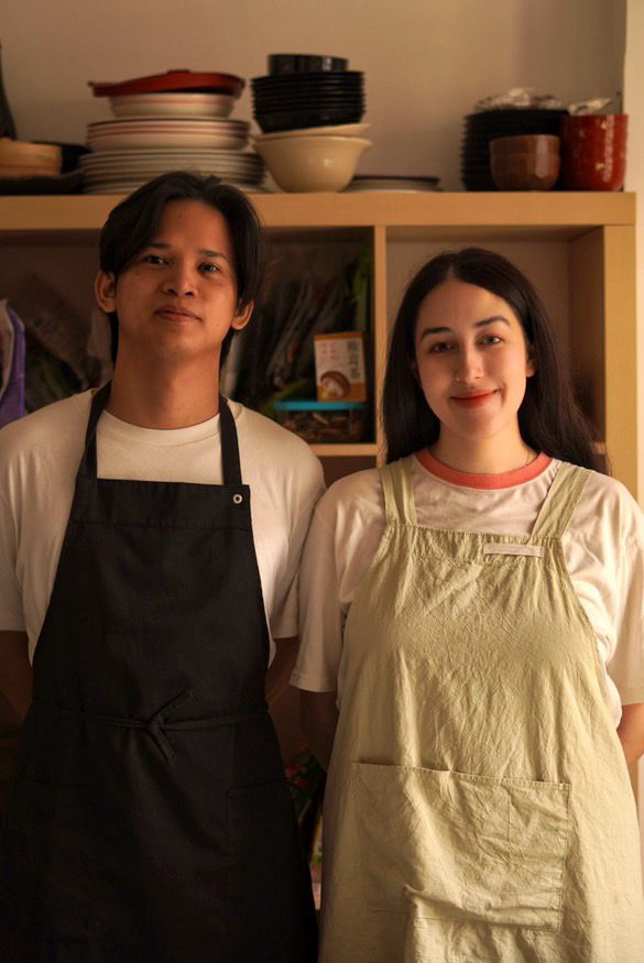 Sara e Levi, fondatori di Tabete Market, sorridono in cucina con i loro grembiuli, pronti a guidare il laboratorio di cucina giapponese sugli onigiri.